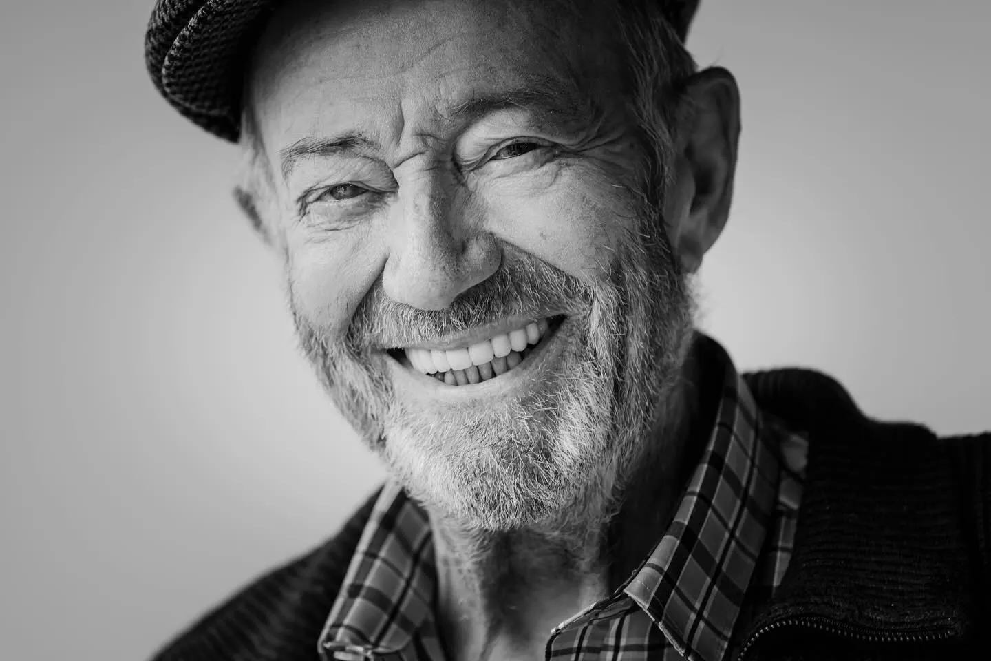 Portrait en noir et blanc de Benoît Allemane, comédien voix off, souriant, casquette et chemise à carreaux