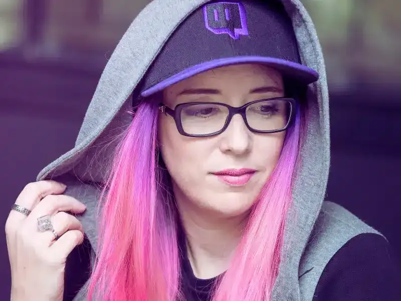 Cécile Heredia, comédienne voix off, cheveux roses, lunettes et casquette Twitch sous sa capuche