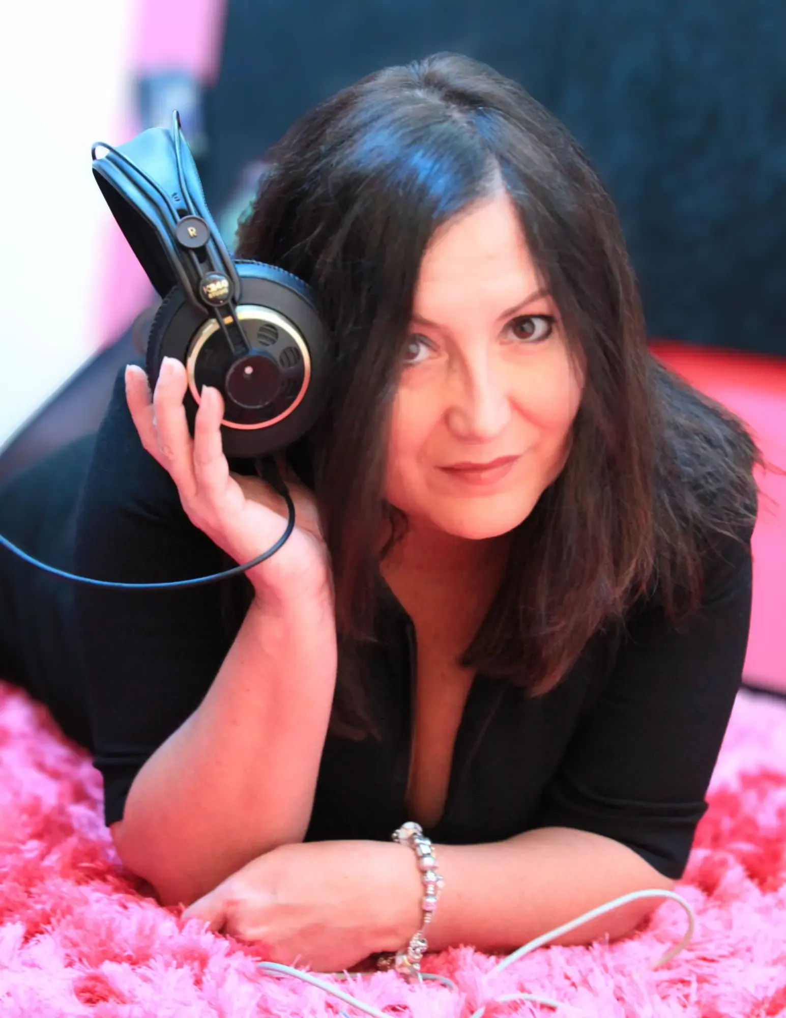 Estelle Hubert smiling, lying on a pink rug with studio headphones in her hand