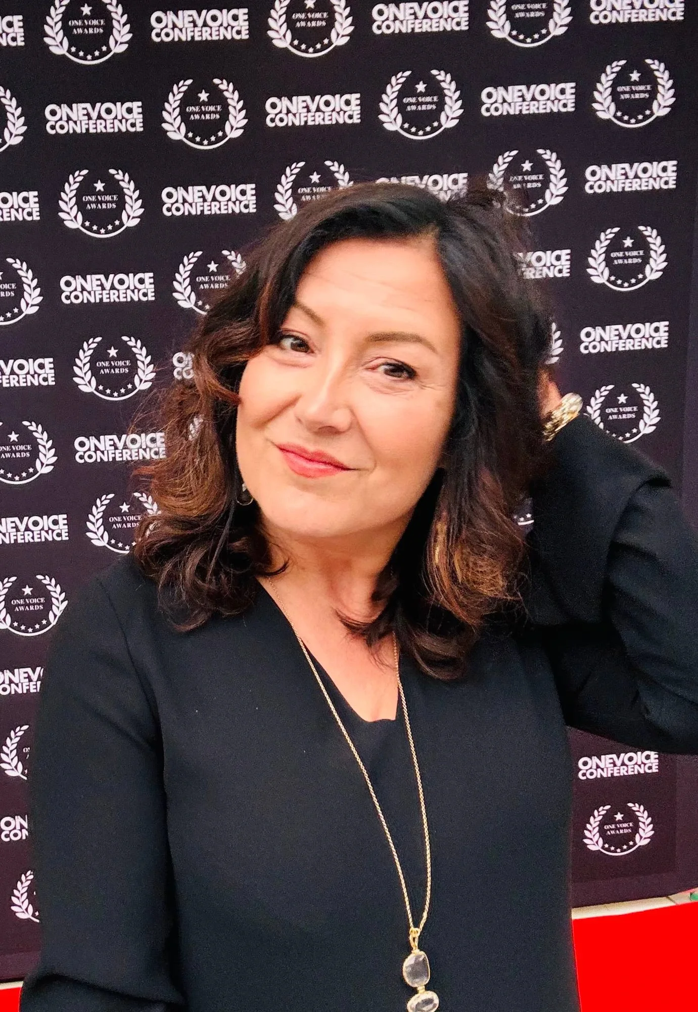 Estelle Hubert, award-winning French voice actor at the One Voice Awards, smiling in black in front of the One Voice Conference press wall