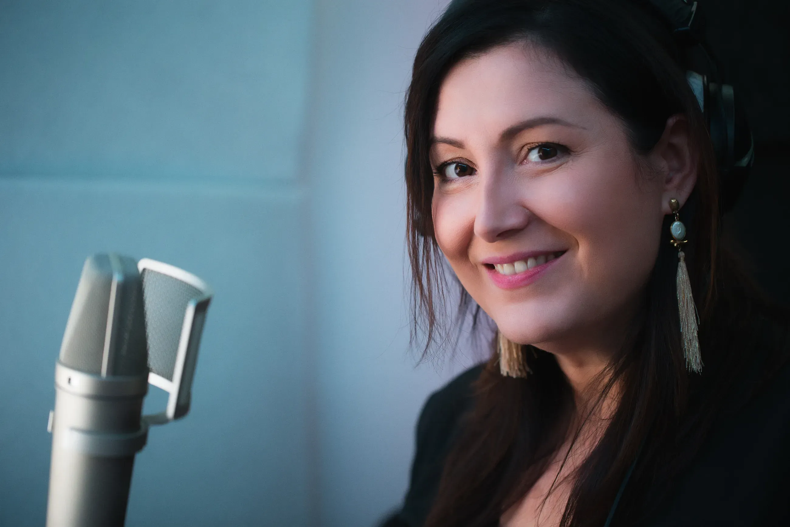 Voice actor Estelle Hubert smiles beside her Neumann U87 microphone in her studio booth