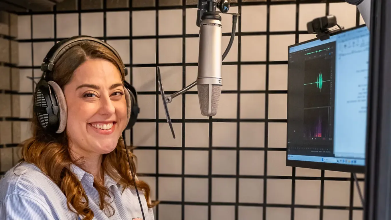 Stephanie Matard, comédienne voix off anglaise, souriante dans sa cabine d’enregistrement, casque sur les oreilles, devant son micro