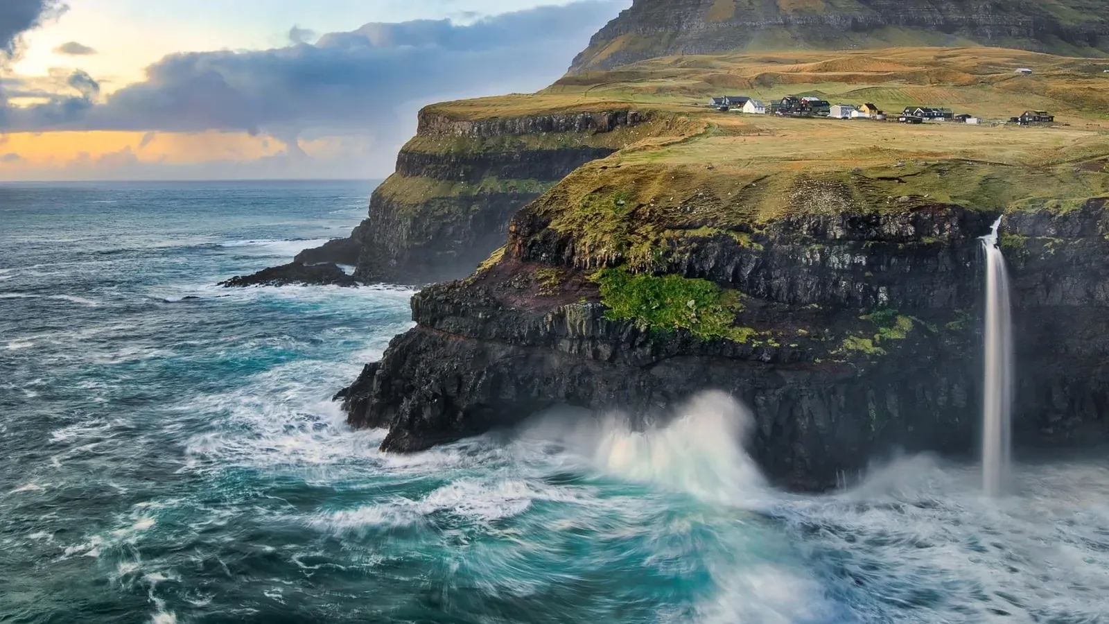 Falaises verdoyantes des îles Féroé, une cascade plonge dans l’océan agité