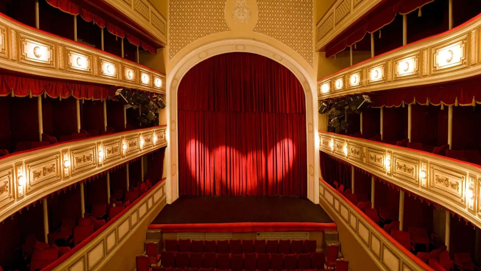 An Italian-style theatre with gilded balconies and a lit red curtain