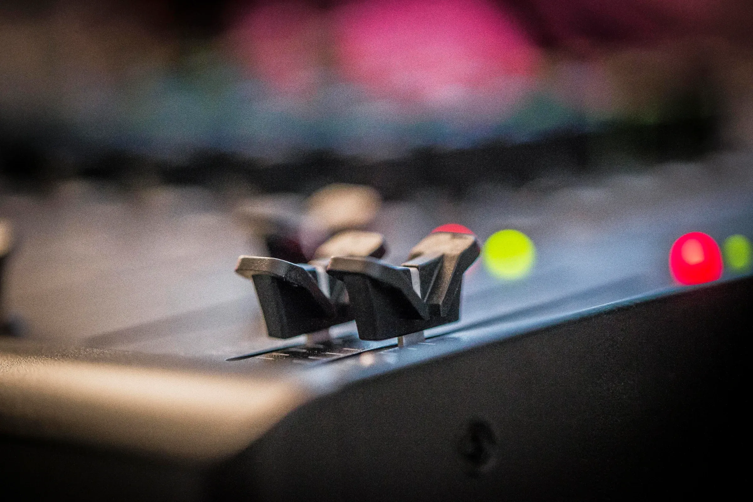 Gros plan sur deux faders d’une table de mixage, voyants en arrière-plan