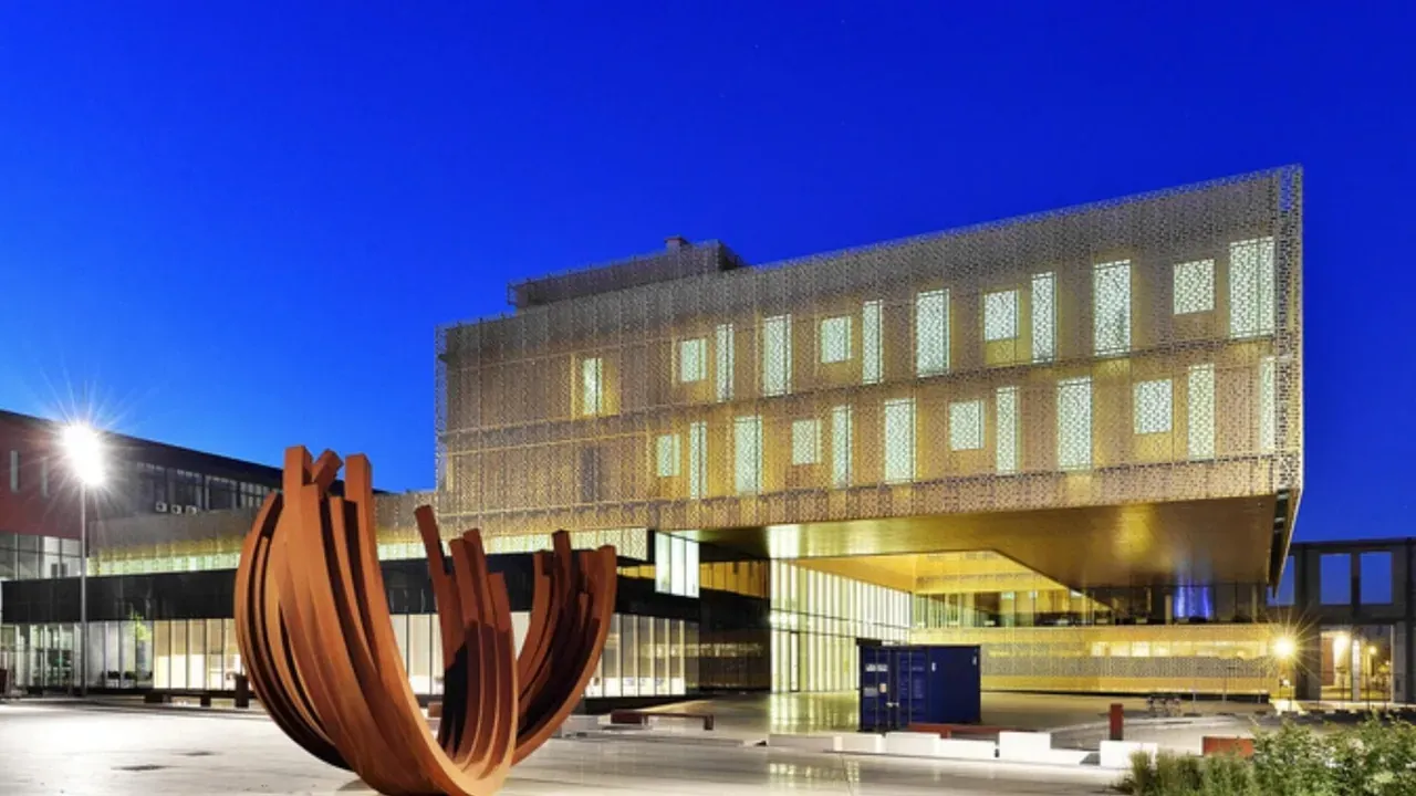 The glass façade of CMI’s L’Orangerie illuminated at dusk, with a steel sculpture in the foreground