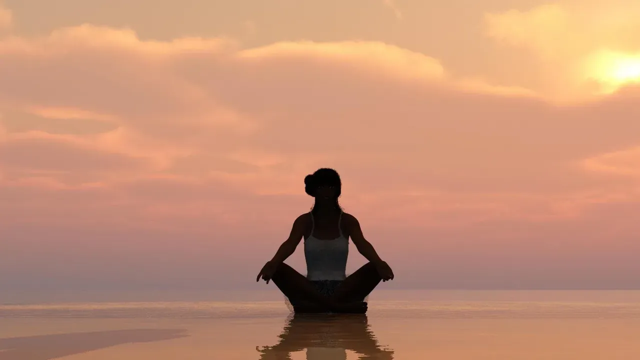 A silhouette meditating by the water at sunset