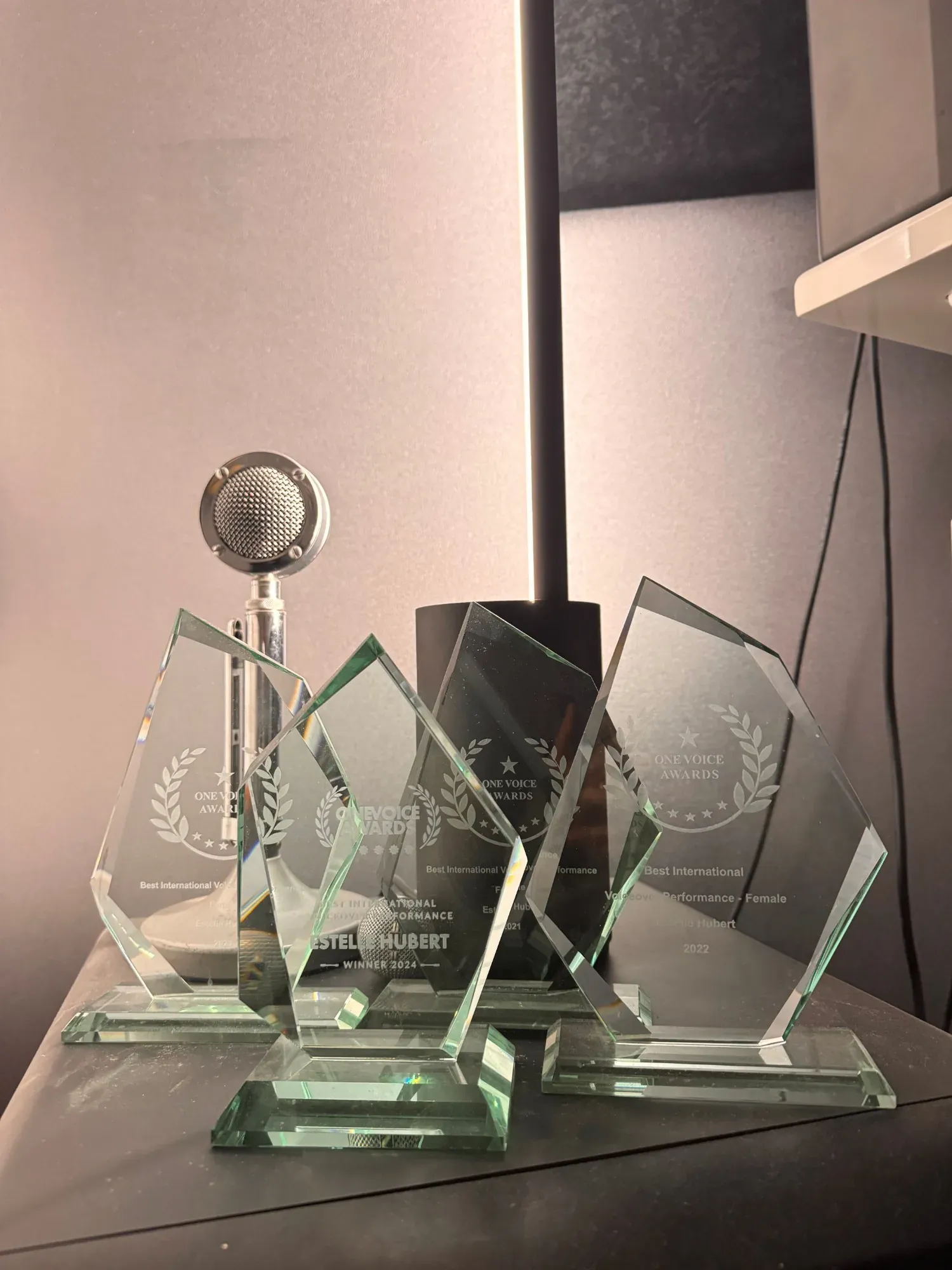 The four glass One Voice Awards trophies won by voice actor Estelle Hubert, beside a vintage microphone