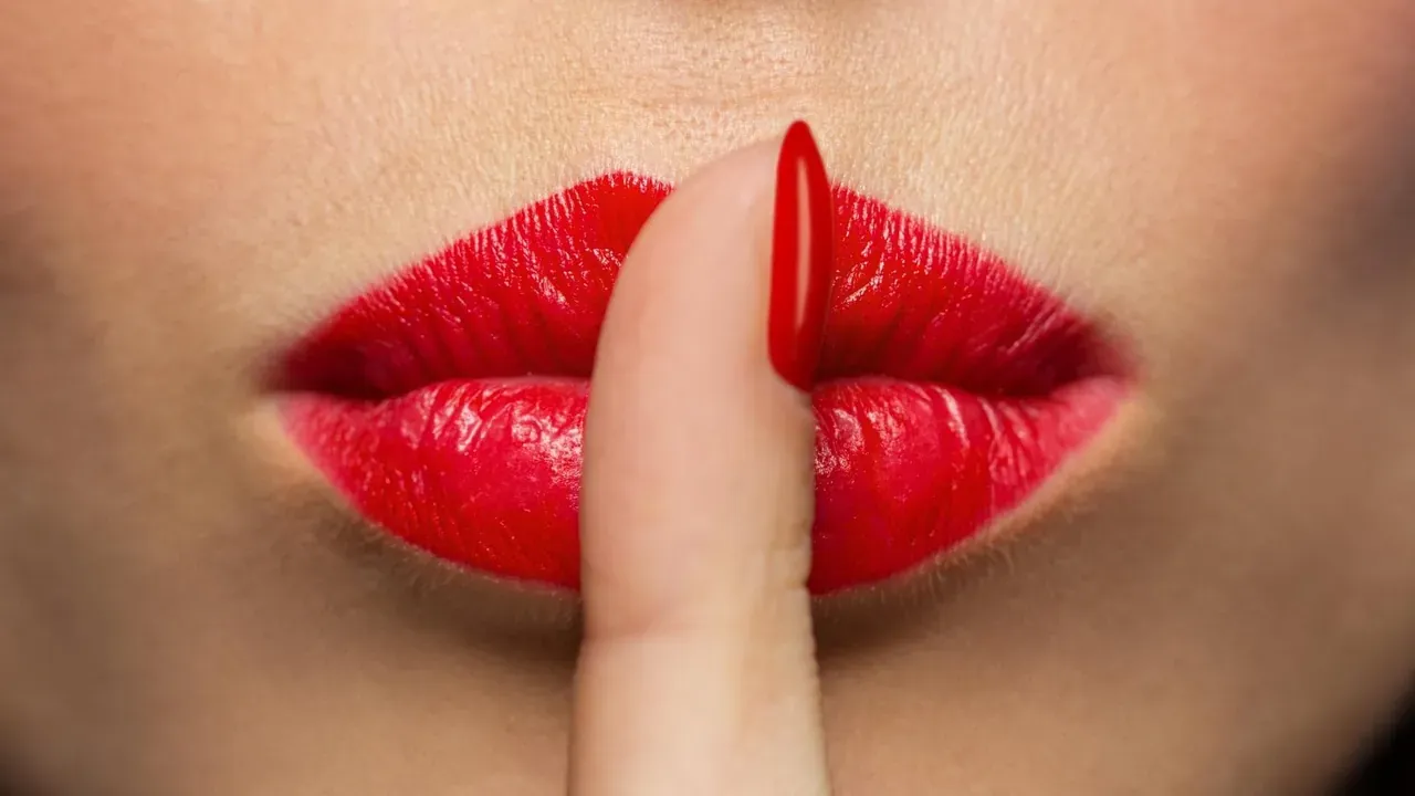 Lèvres rouges en gros plan, un doigt posé en signe de silence