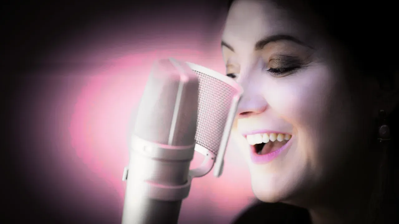 Estelle Hubert, comédienne voix off, rit au micro Neumann dans sa cabine, en lumière rose