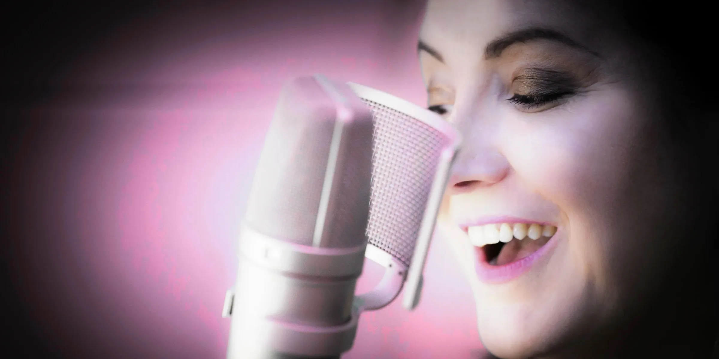 Estelle Hubert smiling with her eyes closed at the microphone in her home studio, lit in pink