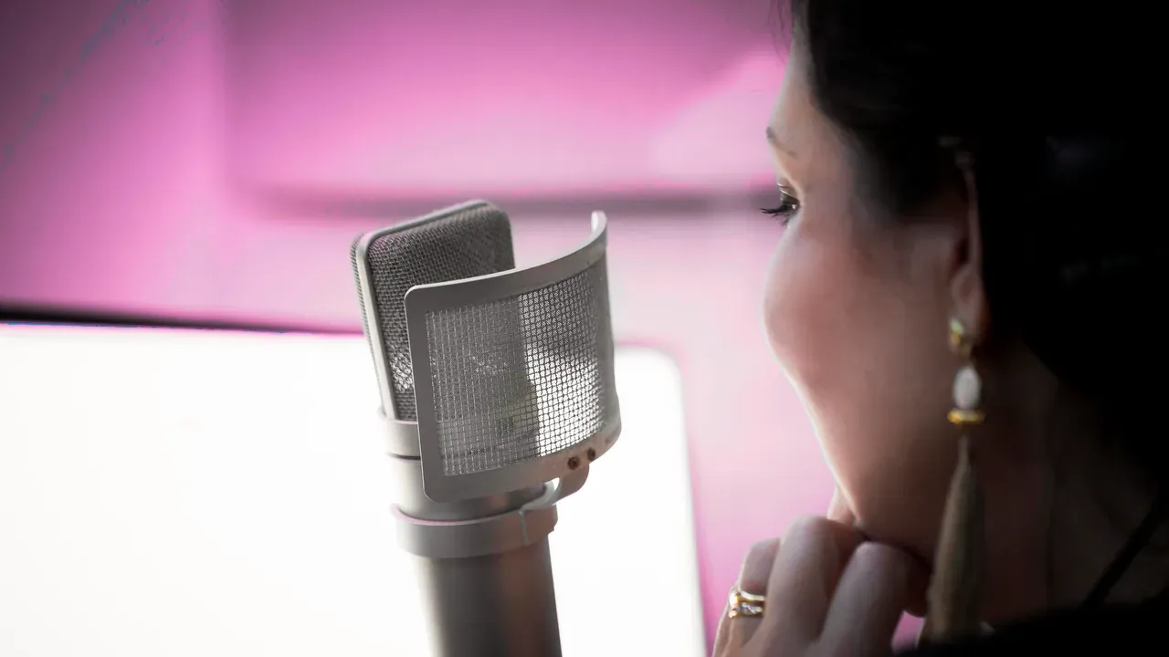 Estelle Hubert à l’écoute devant le micro Neumann, la main sous le menton, dans sa cabine en lumière rose