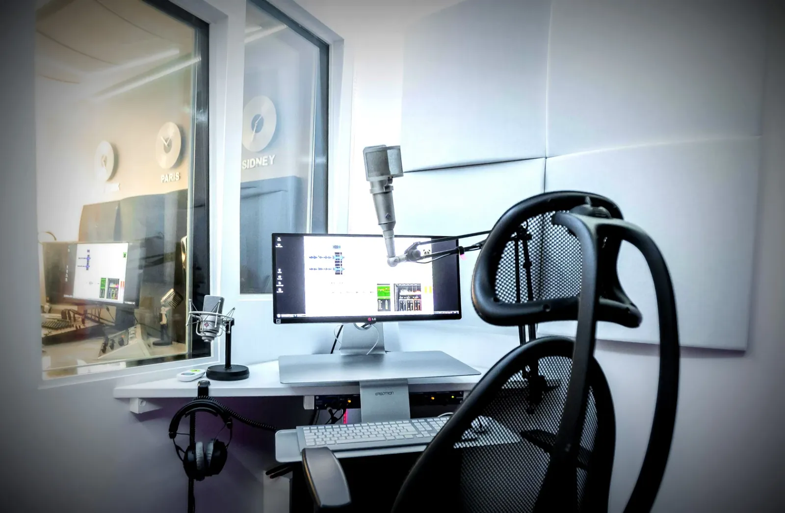 Estelle Hubert’s home studio booth, with a microphone on a boom arm, screen, headphones and chair, looking into the control room