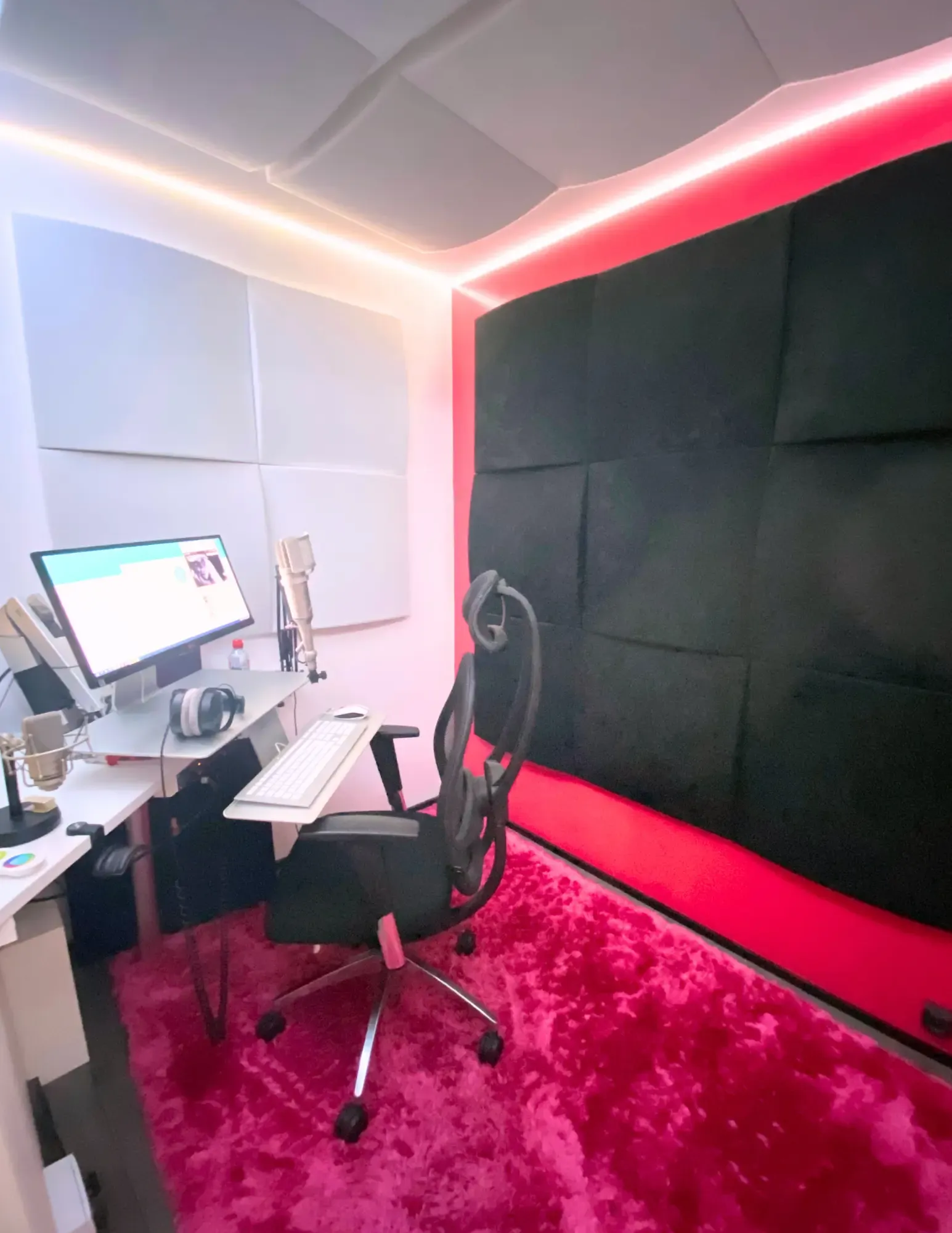 The main studio’s booth: black acoustic panels on a red wall, a pink rug, microphone, screen and headphones