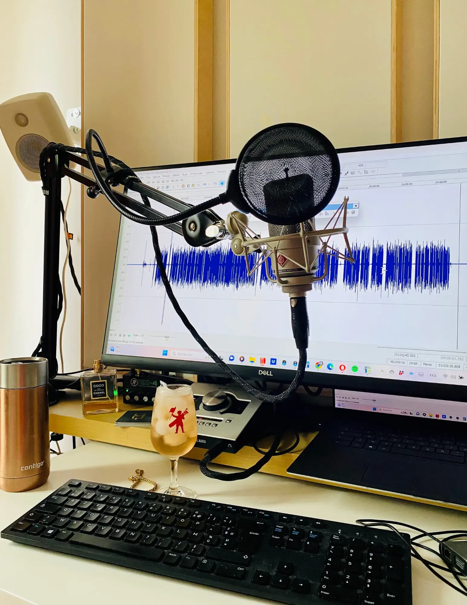 A shock-mounted Neumann microphone in front of an audio waveform on screen in Studio Bis