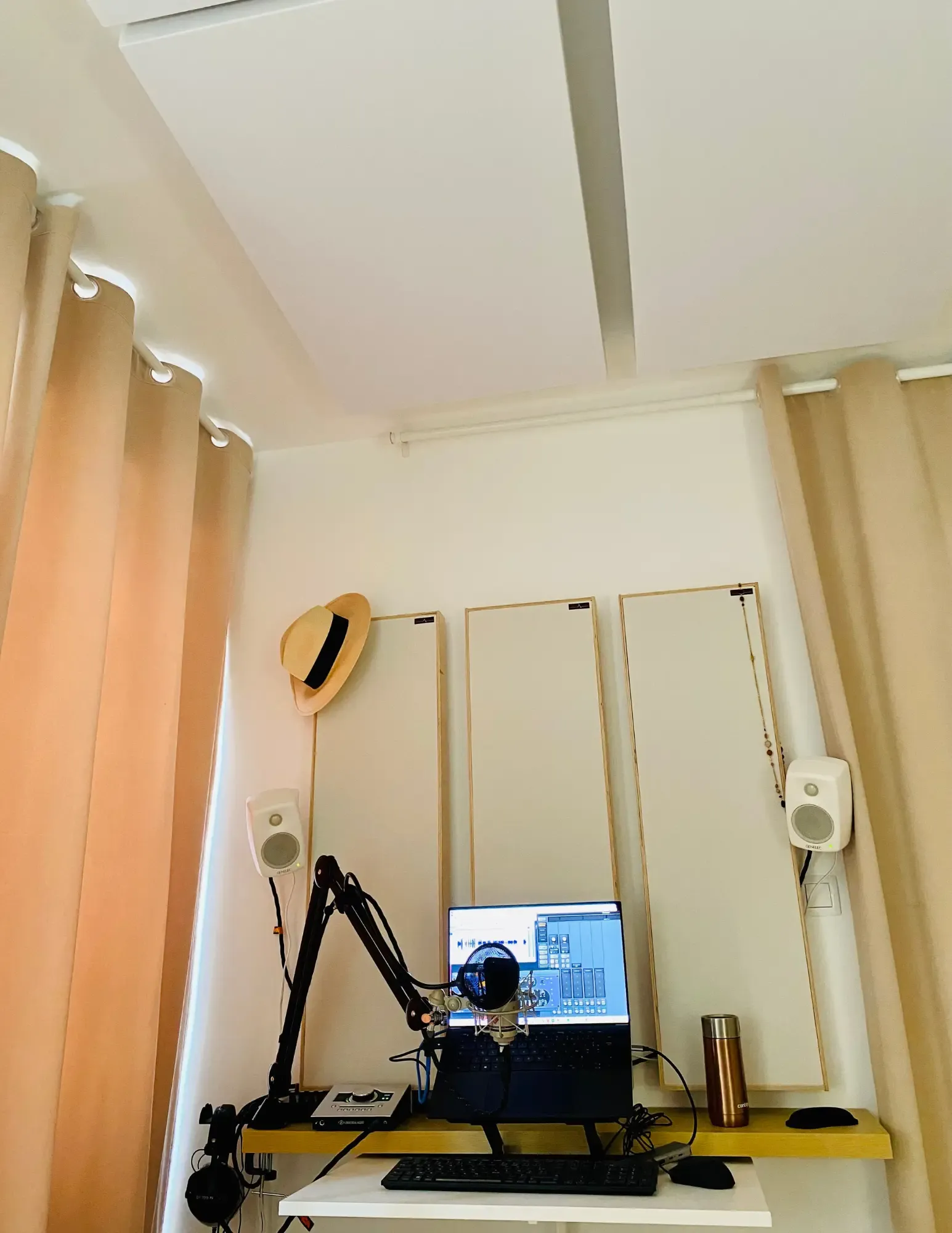 Studio Bis: acoustic panels, two speakers, a shock-mounted microphone in front of the computer and a straw hat on the wall