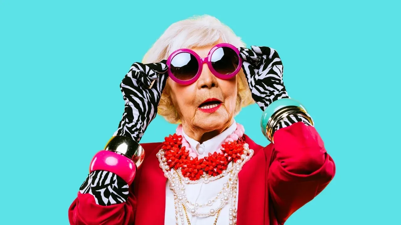 Femme âgée aux lunettes roses et au manteau rouge sur fond turquoise