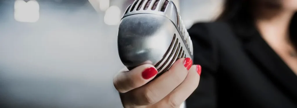 Main d’une femme avec un vernis rouge vif tenant un micro vintage Shure Unidyne, symbolisant la profession de voix off féminine.